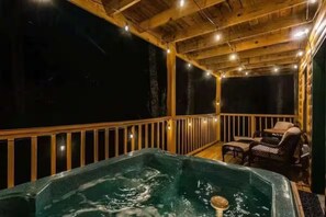 A hot tub in a wooden deck area with string lights, surrounded by wicker furniture. - A Little Bit of Country by Beyond Expectations (Pigeon Forge)
