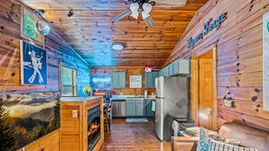 A cozy cabin interior with wooden walls, a fireplace, a kitchen area, and a dining table. - A Little Bit of Country by Beyond Expectations (Pigeon Forge)