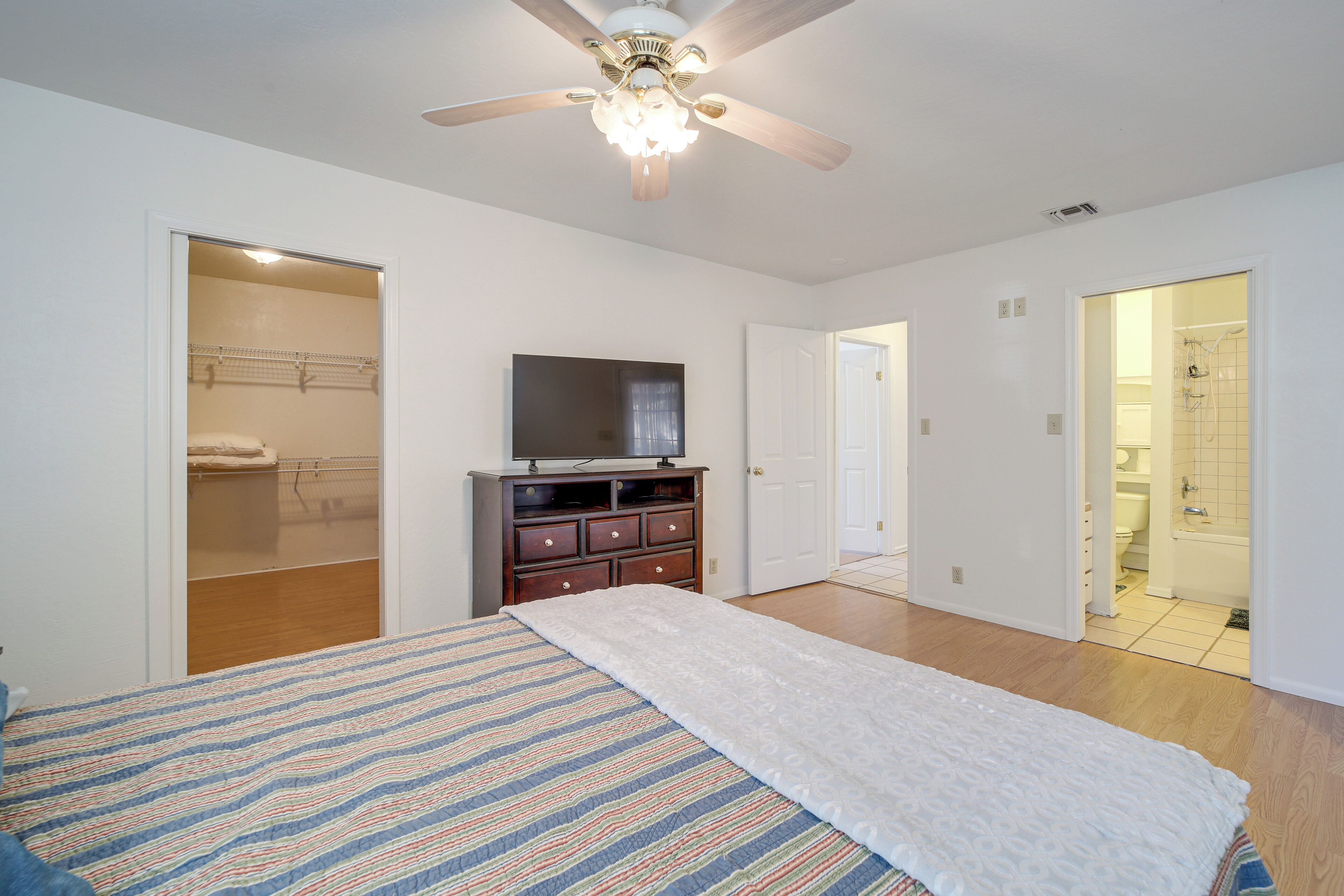 A bedroom with a bed, a ceiling fan, a TV, and a walk-in closet.