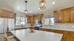 Une cuisine moderne avec des meubles en bois, un grand îlot central, des appareils électroménagers en acier inoxydable et un mur de fond en briques.