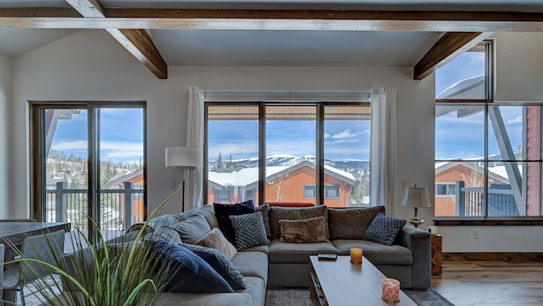 Ett modernt vardagsrum med en hörnsoffa, ett soffbord och stora fönster med utsikt över snötäckta hus.