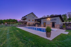 A two-story house with a swimming pool, outdoor seating, and a stone facade.