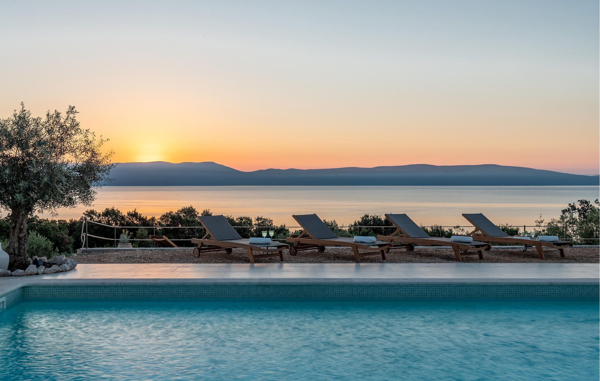 A poolside area with lounge chairs and a view of the sunset over a body of water.