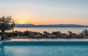 Un espace aménagé au bord de la piscine, avec des chaises longues et une vue sur le coucher de soleil se reflétant sur l’eau.