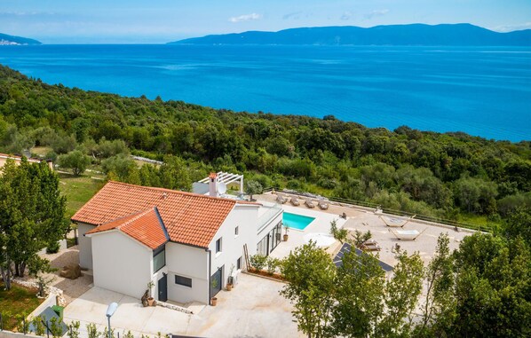Une villa moderne dotée d’une piscine, entourée d’une végétation luxuriante et offrant une vue sur une vaste étendue d’eau.