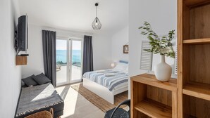 A modern bedroom with a bed, a sofa, a TV mounted on the wall, and a view of the sea through the sliding glass door. - Amazing home in Ravni with sauna (Ravni)