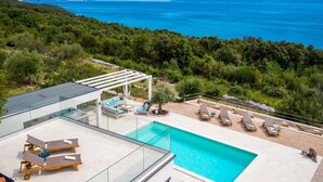 A modern outdoor pool area with lounge chairs and a pergola, overlooking a mountainous coastline. - Amazing home in Ravni with sauna (Ravni)