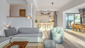 A modern living room with a grey sofa, a wooden coffee table, and a bean bag chair. A kitchen with white cabinets and a dining area with a table and chairs is visible through an open door. - Amazing home in Ravni with sauna (Ravni)