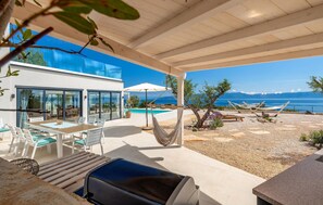 Une terrasse extérieure moderne, dotée d’une piscine, de coins salon et offrant une vue sur la mer.