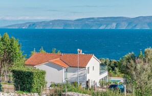 Une maison située sur la côte, avec un toit recouvert de tuiles rouges, des murs blancs et une vue dégagée sur la mer et les collines lointaines.