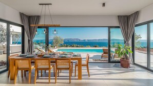 A dining area with a table set for four, overlooking a pool and a scenic view of the sea and mountains. - Amazing home in Ravni with sauna (Ravni)