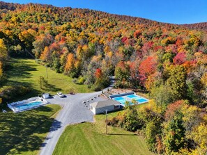 Ein Wohngebiet mit Schwimmbad, umzäunter Garten und einer Straße, die zu einem Hügel mit Herbstlaub führt.