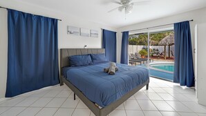 Un dormitori amb un llit, un ventilador de sostre i vista a una piscina exterior.