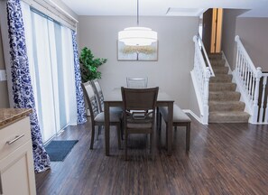 Un coin repas avec une table et des chaises, une plante en pot et un escalier avec des rampes blanches.
