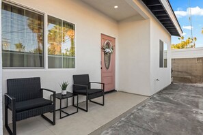 A house exterior with a porch, two chairs, a small table, and a potted plant.
