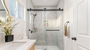 Un baño moderno con ducha envuelta en vidrio, inodoro y lavamanos con una orquídea en maceta.