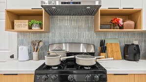 A modern kitchen with a gas stove, pots, a toaster, and wooden shelves with decorative items. - Anaheim, 2BR, modern guesthouse, Disneyland, sleeps 7, private entry & parking. (Anaheim)