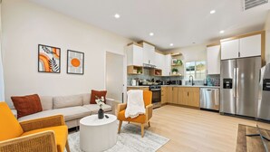 A modern living room with a sofa, armchairs, and a coffee table. Adjacent to the living room is a kitchen with stainless steel appliances and wooden cabinets. - Anaheim, 2BR, modern guesthouse, Disneyland, sleeps 7, private entry & parking. (Anaheim)