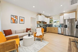 A modern living room with a sofa, armchairs, and a coffee table. Adjacent to the living room is a kitchen with stainless steel appliances and wooden cabinets. - Anaheim, 2BR, modern guesthouse, Disneyland, sleeps 7, private entry & parking. (Anaheim)