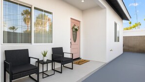 A modern exterior with two black wicker chairs, a small table, and a potted plant on a white porch. - Anaheim, 2BR, modern guesthouse, Disneyland, sleeps 7, private entry & parking. (Anaheim)
