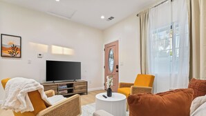 Una sala de estar moderna con un televisor de pantalla plana, un sofá, dos sillones, una mesa de centro y una puerta con un panel de vidrio decorativo.