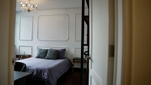 Um quarto com cama, uma cadeira, uma escrivaninha e um candelabro.