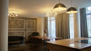 Uma sala de jantar com mesa e cadeiras de madeira, um lustre e um sofá.