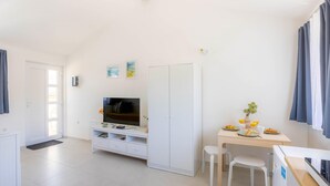 Ein moderner, gut beleuchteter Raum mit Fernseher, Kleiderschrank, Esstisch mit Stühlen und einer kleinen Pflanze.