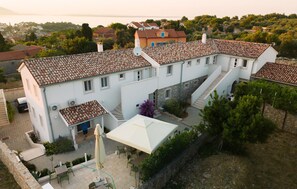 A white building with a tiled roof, a staircase, and a patio area with chairs and an umbrella. - 1 bedroom amazing apartment in Veli Losinj (Veli Losinj)