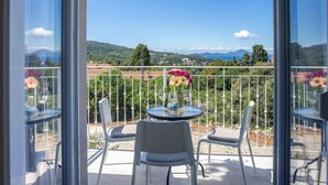 A balcony with a table and chairs, a vase of flowers, and a scenic view of mountains and a coastline. - 1 bedroom amazing apartment in Veli Losinj (Veli Losinj)