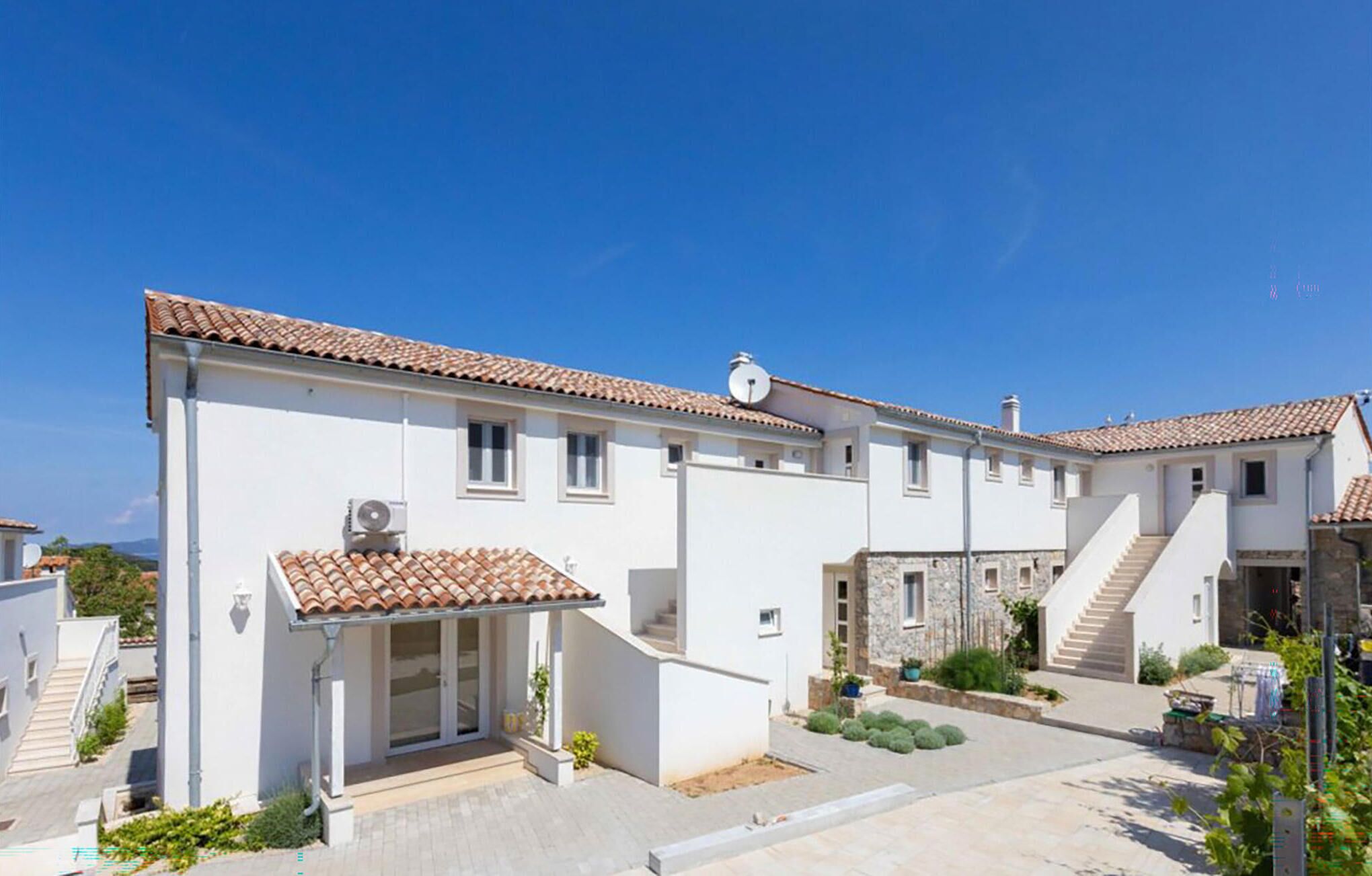 Un edificio moderno su due piani con tetto in tegole, ingresso coperto e un piccolo giardino.