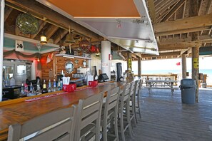 A beachside bar with wooden beams, a counter with various bottles, and a view of the ocean. - Beachfront Bliss with Panoramic Gulf Views | Sandpiper Cove 2152 Destin, FL (Destin)