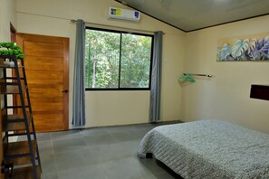 Une chambre à coucher avec un lit, une porte en bois, une fenêtre avec des rideaux, un climatiseur fixé au mur et un tableau.