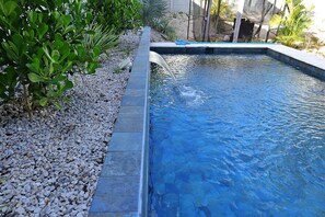Une piscine dont l’eau est d’un bleu cristallin, entourée d’un bord de galets et d’une végétation luxuriante.