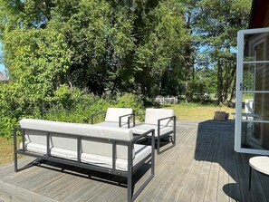 Eine Terrassensitzgruppe im Freien mit einer Couch und Stühlen, umgeben von viel Grün.