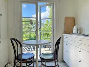 A room with a table and two chairs, a kitchenette with a coffee maker, and a view of greenery outside. - 6 Person Holiday Home in Lottorp (Löttorp)