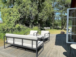 A wooden deck with outdoor furniture, surrounded by lush greenery.