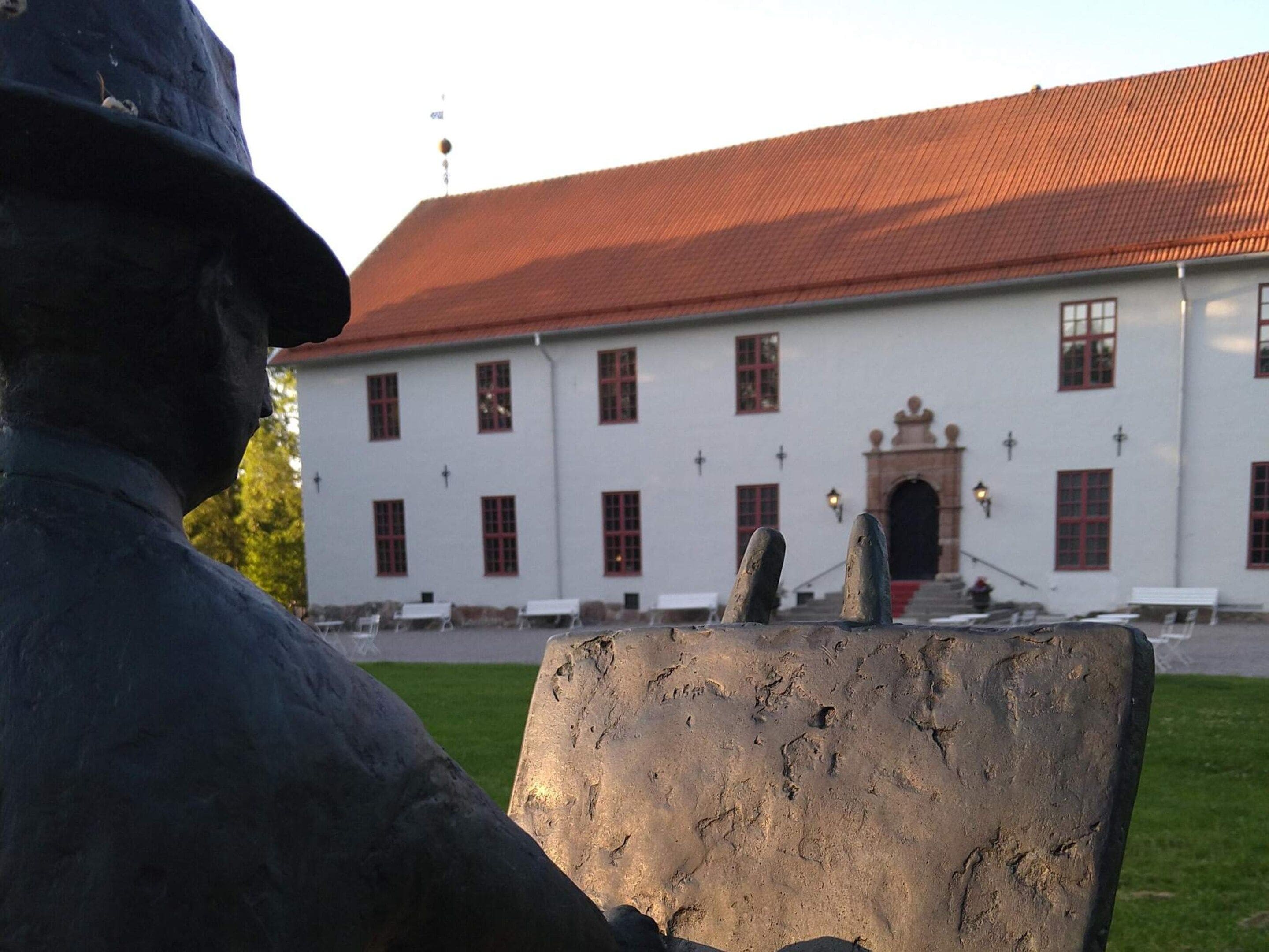 A statue in front of a building with a red roof and multiple windows.