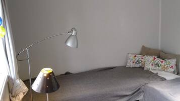 A bedroom with a bed, a desk, a lamp, and a window with curtains.