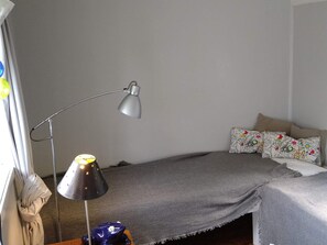 Quarto com cama, escrivaninha, luminária e janela com cortinas.