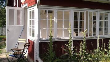 A red building with a white windowed porch, a door, and a chair outside.