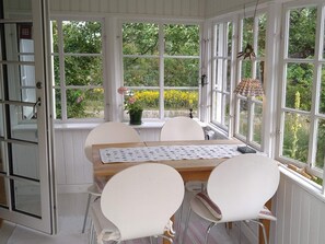 Uma estufa com mesa e cadeiras, amplas janelas e vista para o verde.