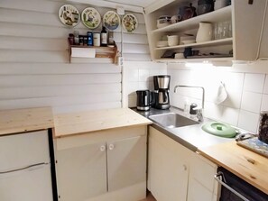 Cozinha com pia, cafeteira e um banquinho verde.