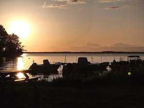 Vista do pôr do sol sobre a água, com barcos atracados e um píer que se estende até a água.