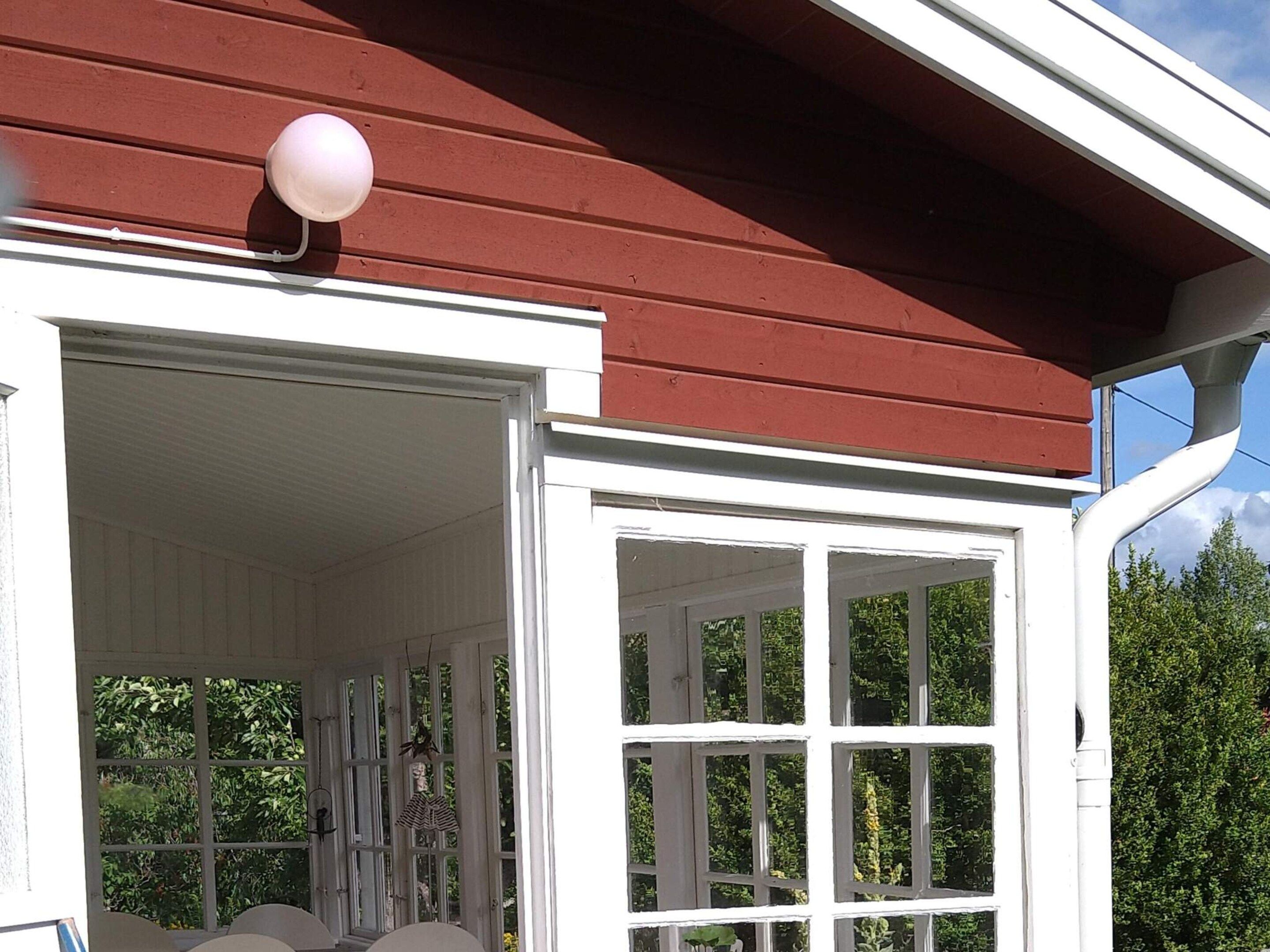 A white porch with a red roof, a white door, and a window with a view of greenery.