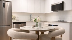 A modern kitchen with white cabinetry, stainless steel appliances, and a round dining table with two chairs. - Fully Furnished Stylish Vaughan Condo near / Steps to VaughanMills (Vaughan)