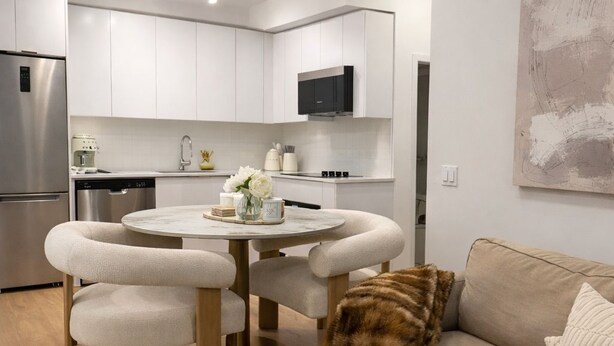 A modern kitchen with white cabinets, a stainless steel refrigerator, and a dining area with a round table and four chairs. - Fully Furnished Stylish Vaughan Condo near / Steps to VaughanMills (Vaughan)