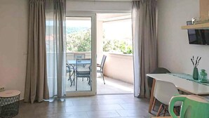 A room with a sliding glass door leading to a balcony with a table and chairs, a small round table with a chair, and a television mounted on the wall. - Lovely apartment in Rab with WiFi (Rab)