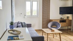 Een moderne woonkamer met een bank, salontafel, stoel, televisie en raam.