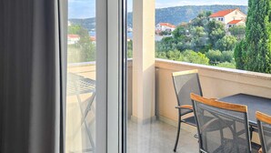 Een balkon met een tafel en stoelen, met uitzicht op een heuvel met gebouwen en begroeiing.